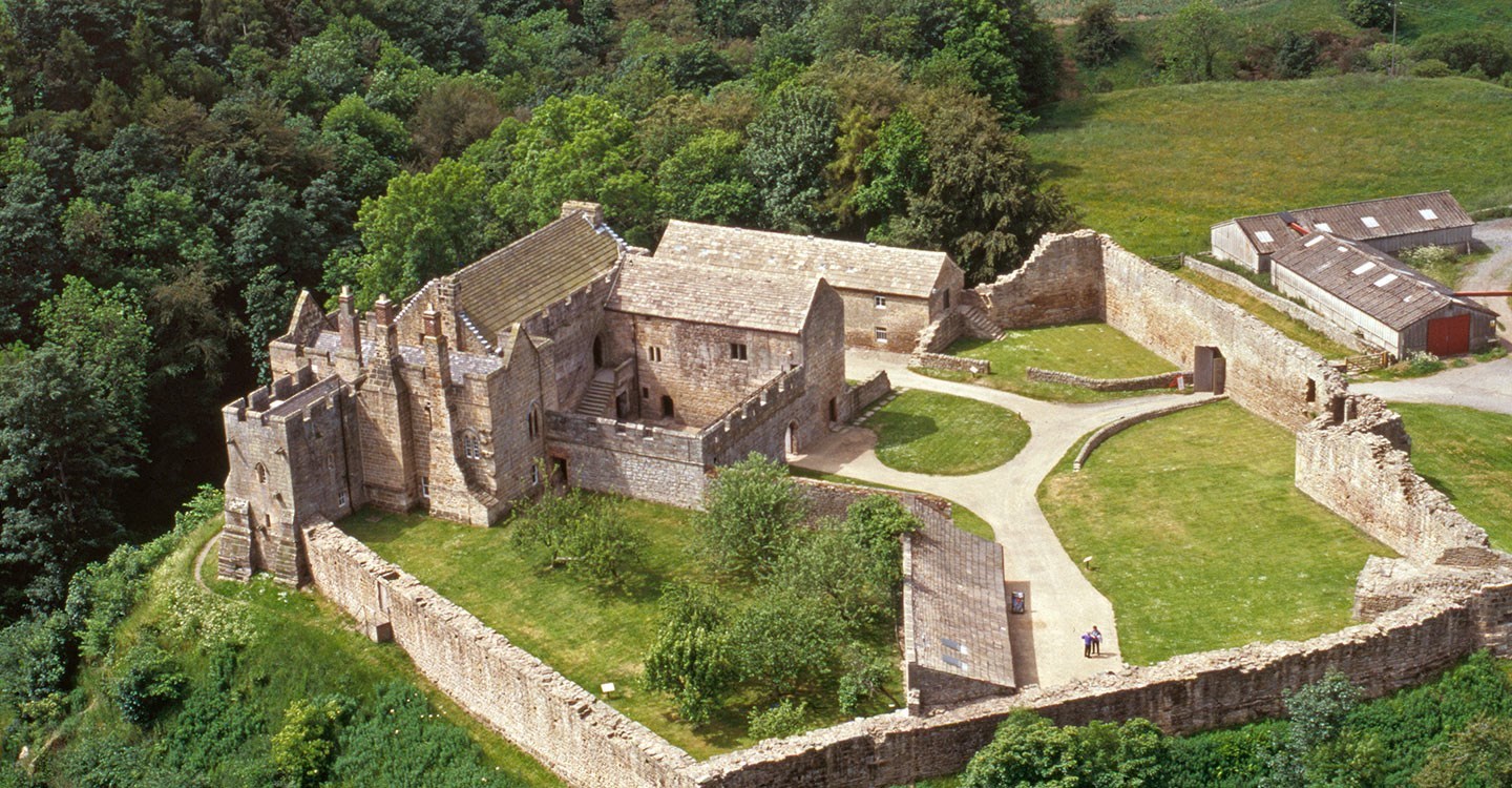 Aerial view of the substantial remains of Aydon Castle perched on the edge of scarp above Cor Burn