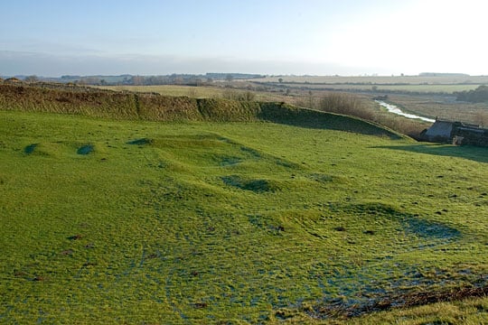 Outlines of buildings in the outer bailey, visible in low relief below the grass