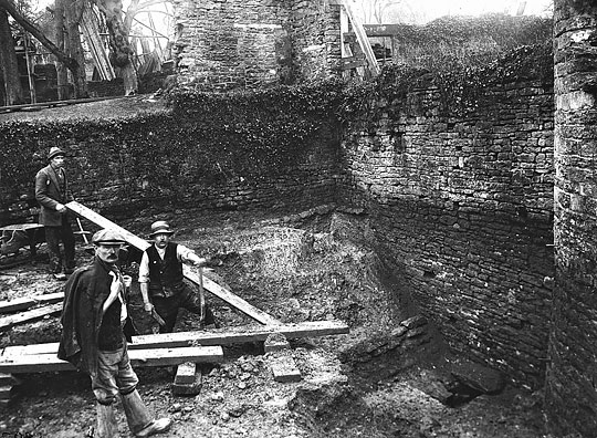 Black and white photograph of the excavation of the south-west tower at Farleigh Hungerford Castle by the Ministry of Works in 1924, with three men digging in waistcoats, jackets and hats