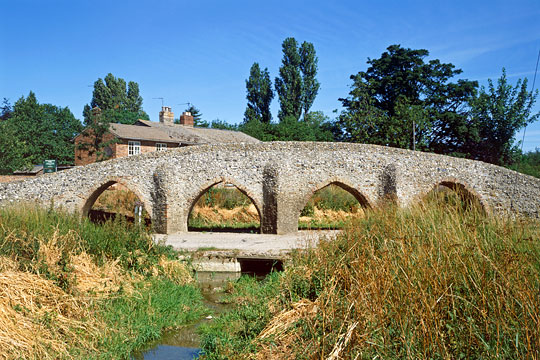 The 15th century bridge from the south with stream in foreground and cottage behind