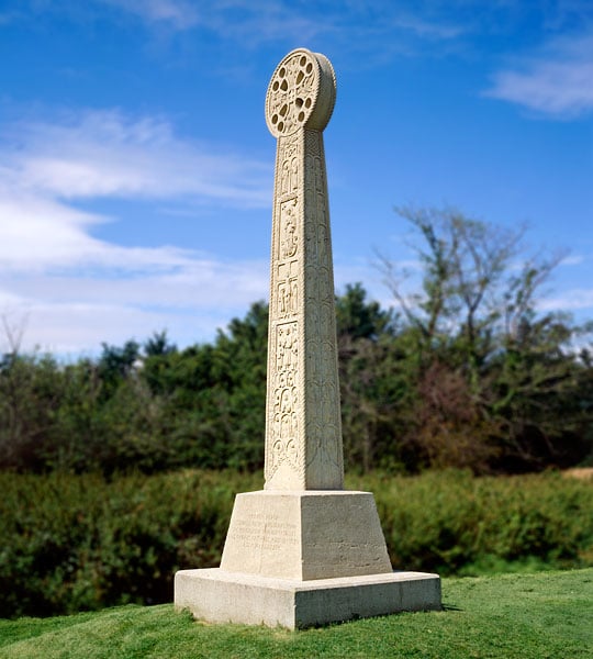 The intricately carved St Augustine's cross, near Minster, set in lawn and backed by shrubs