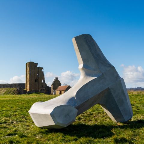 Image of a large sculpture in the shape of a dolos created by Ryan Gander in front of Scarborough Castle on a sunny day