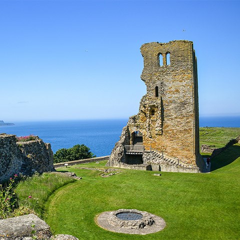 A ruined castle tower surrounded by grass with the sea in the distance on a sunny day (Scarborough Castle) A ruined castle tower surrounded by grass with the sea in the distance on a sunny day (Scarborough Castle)