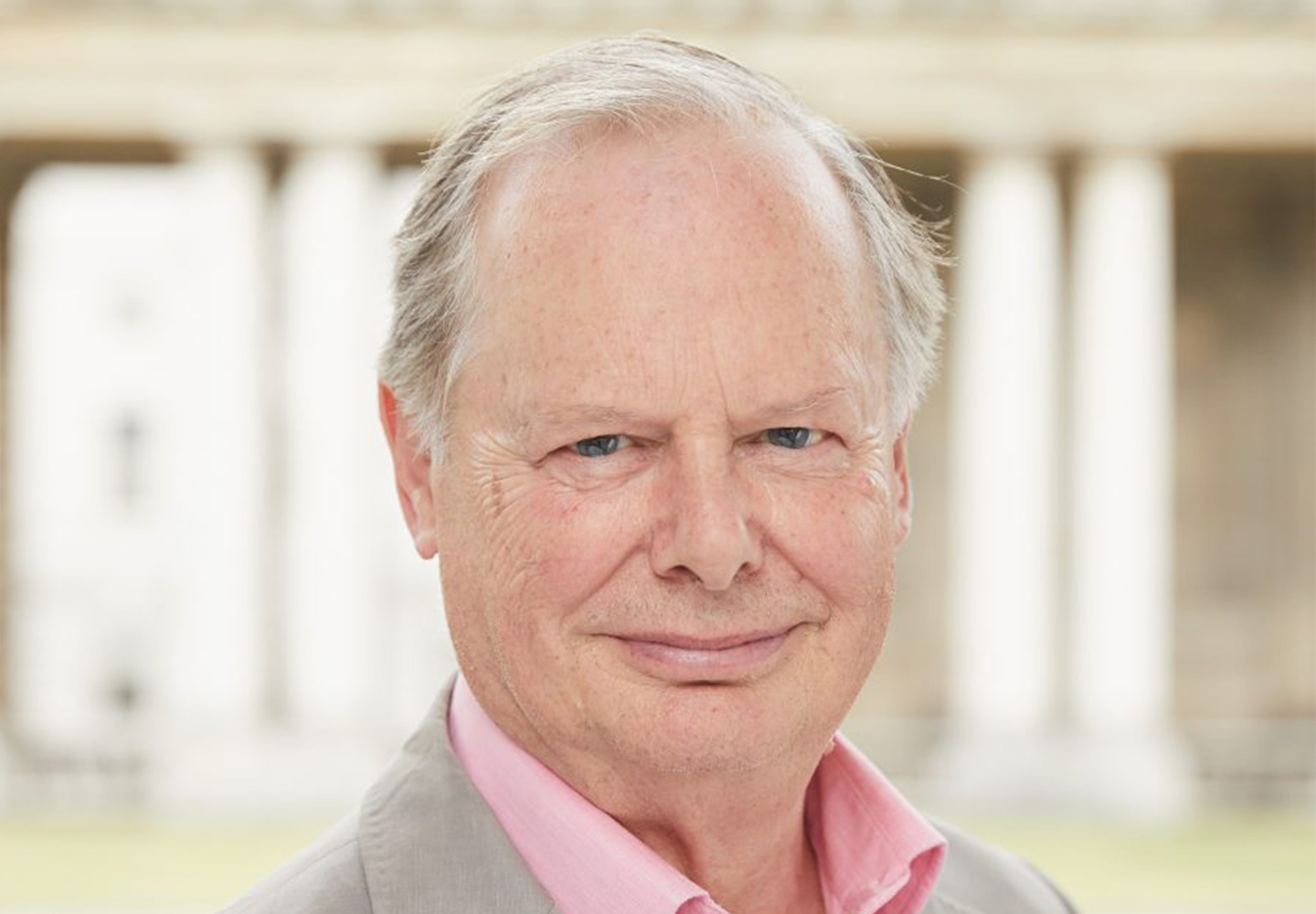 A man (Tony Hales) in pink shirt and white jacket smiles at the camera