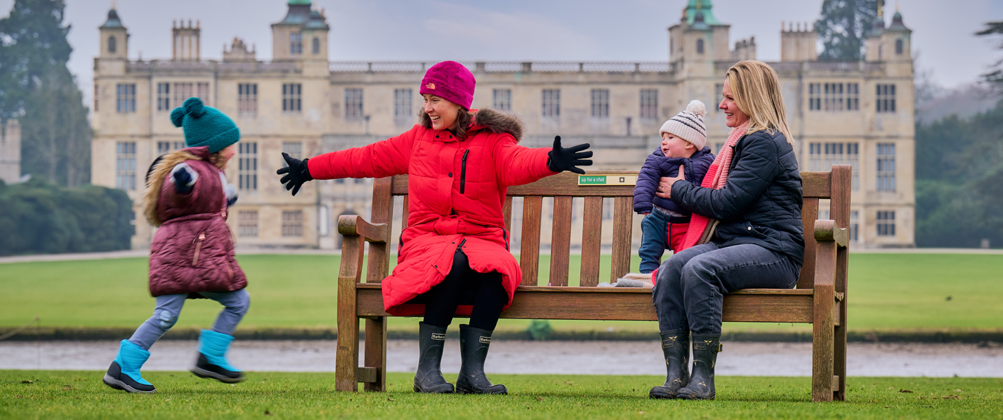 Image: two women are sitting on a bench as a happy child runs towards them 