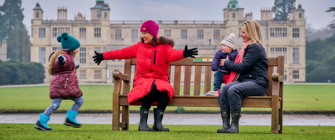 Image: two women are sitting on a bench as a happy child runs towards them Image: two women are sitting on a bench as a happy child runs towards them