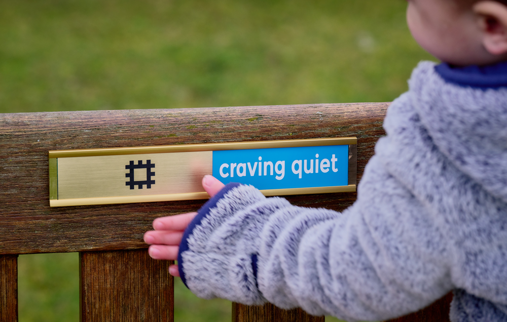 Image: a child looks at the slider on a bench, which says 'craving quiet'