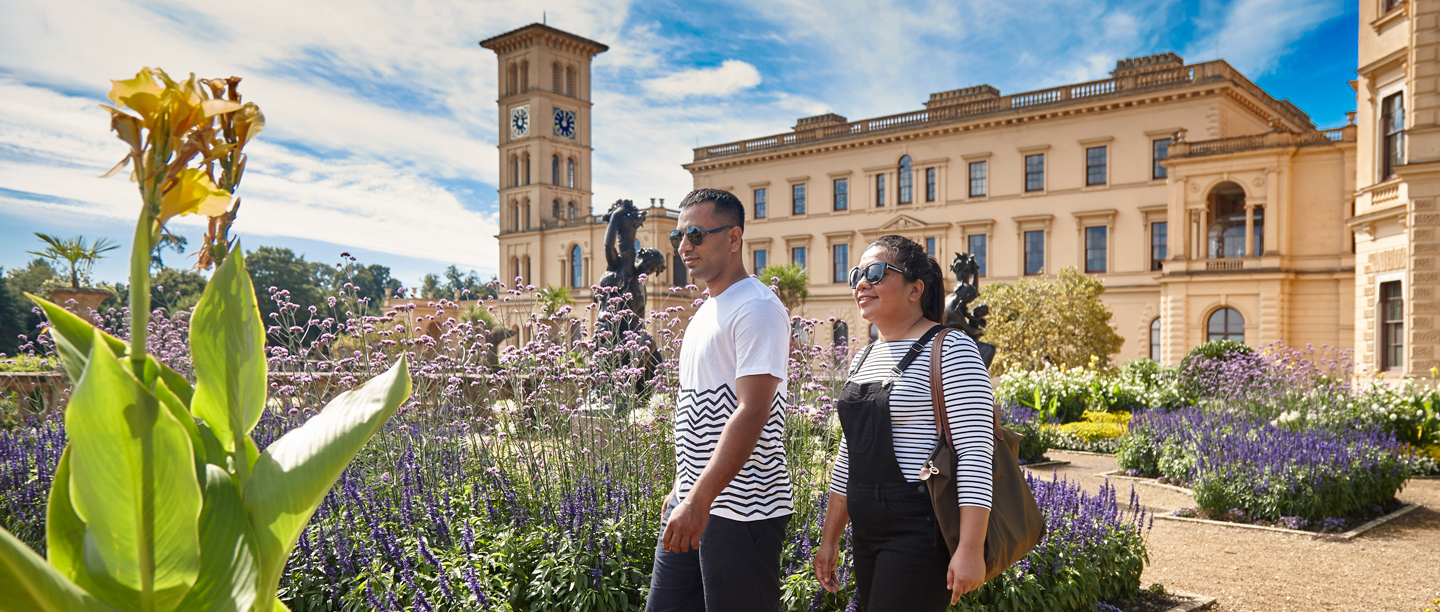 Two adults walk side by side in the gardens at Osborne on a sunny day.