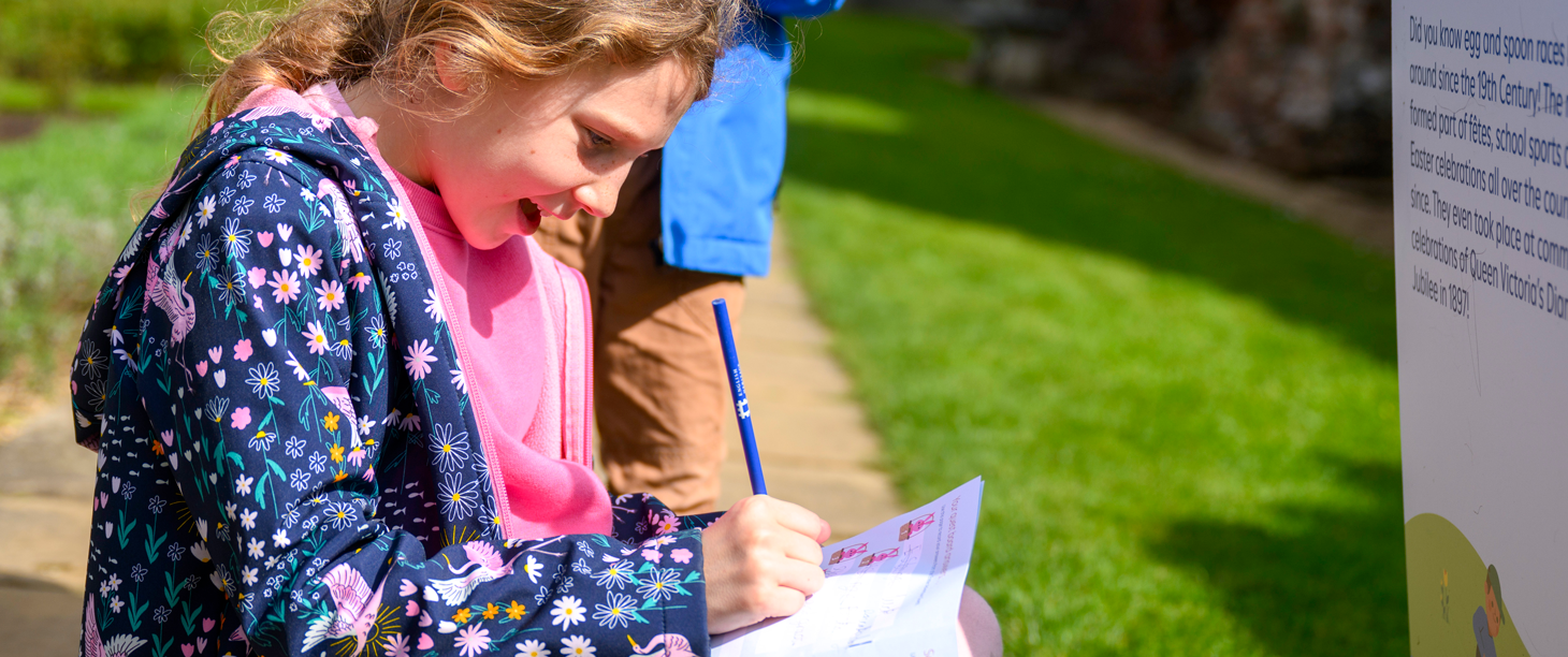 Image: a girl completes an English Heritage adventure quest booklet 