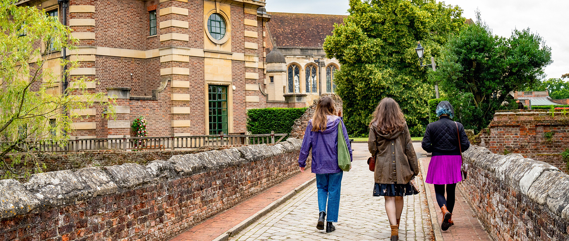 Three adults walk side by side on the stone bridge at Eltham Palace.