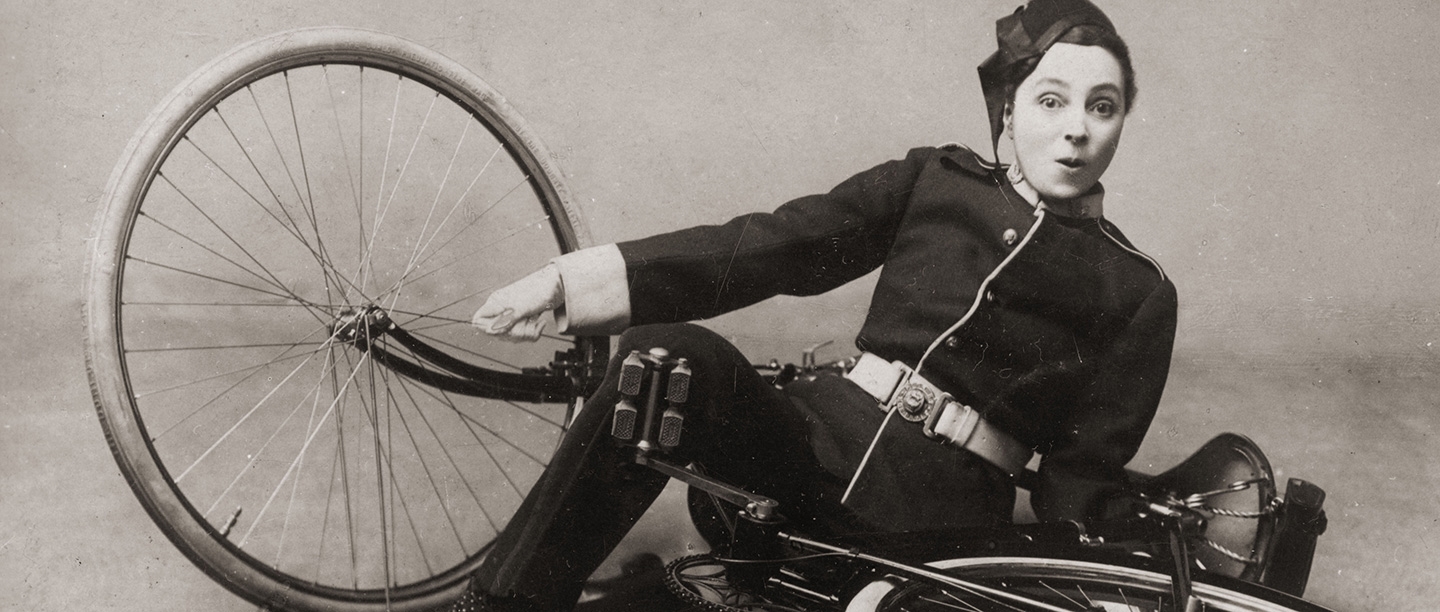 Black and white photograph of Vesta Tilley dressed as a policeman and falling off a bicycle