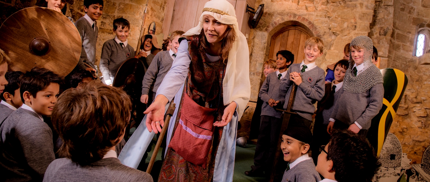 A woman dressed in Saxon costume holds her hands out towards students