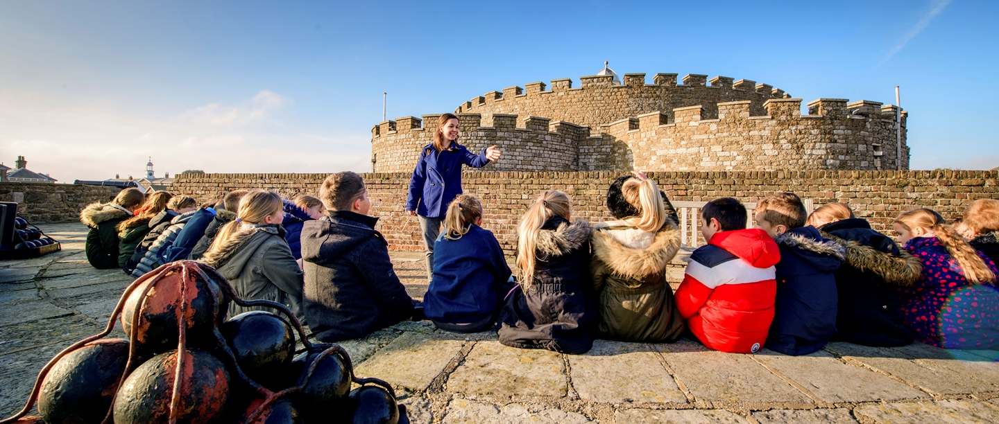 Teacher addresses a large group of students in front of Deal Castle