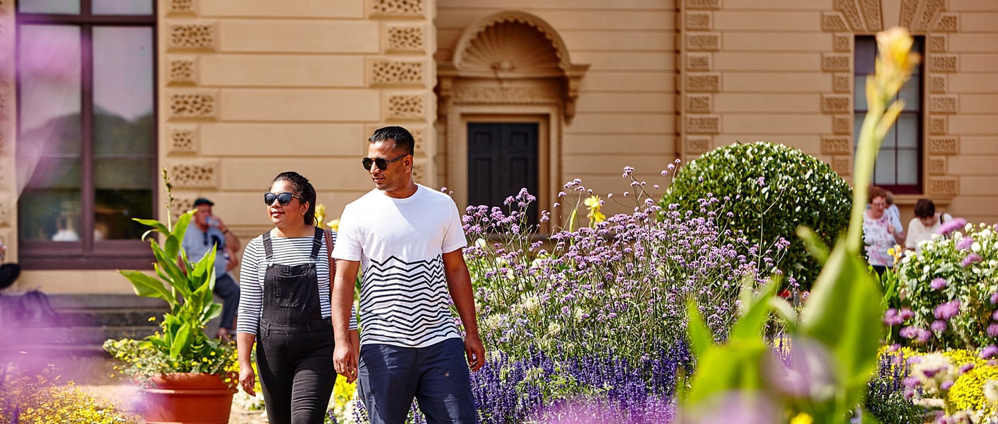 A man and a woman walk through the gardens at Osborne on a sunny day.