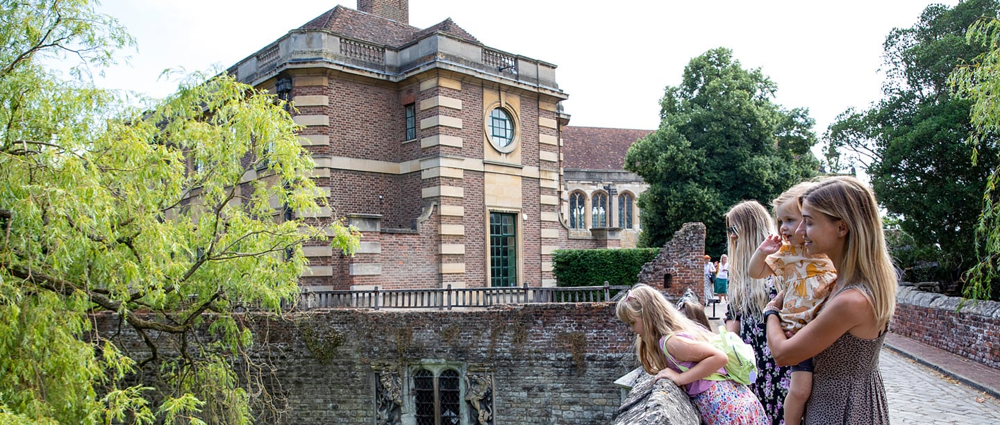 Two women and three children stand on the bridge and look over at the moat and gardens at Eltham Palace.