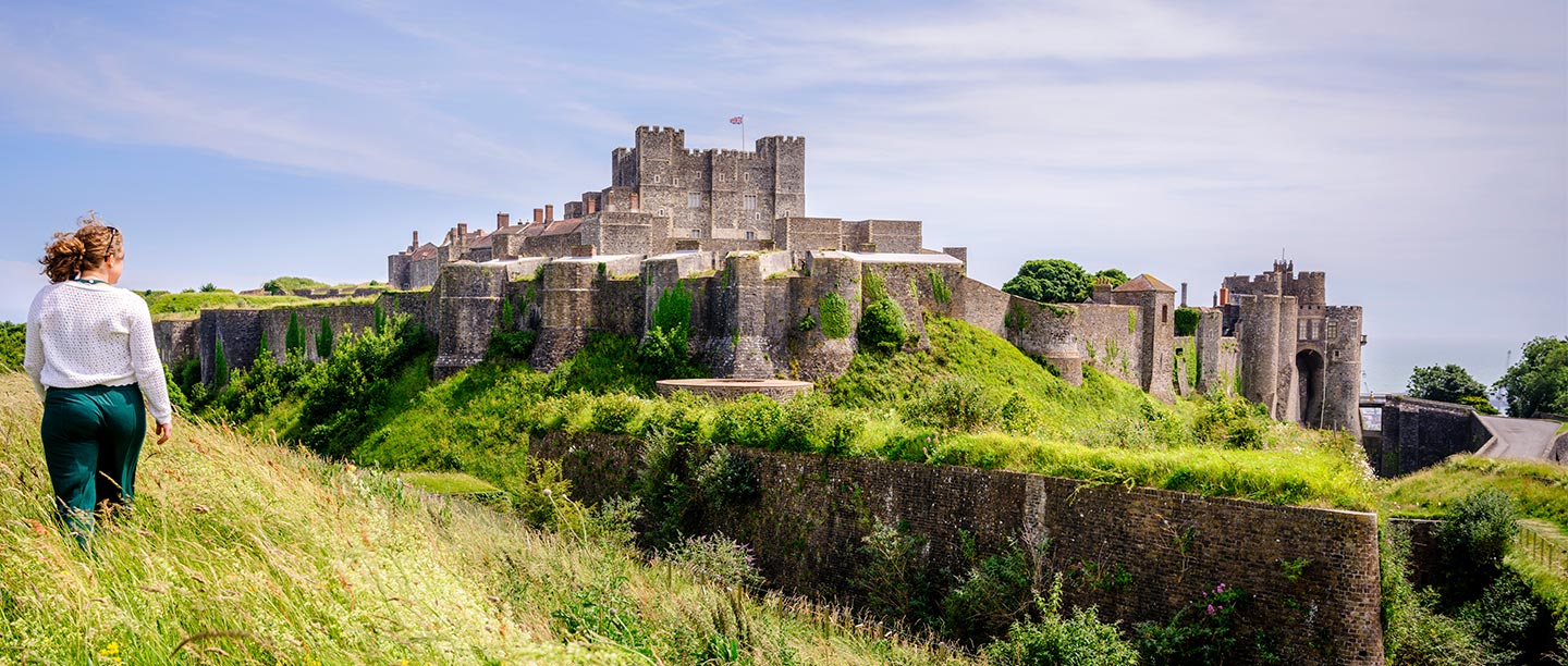 A woman walks in long grass looking at a huge, impressive castle