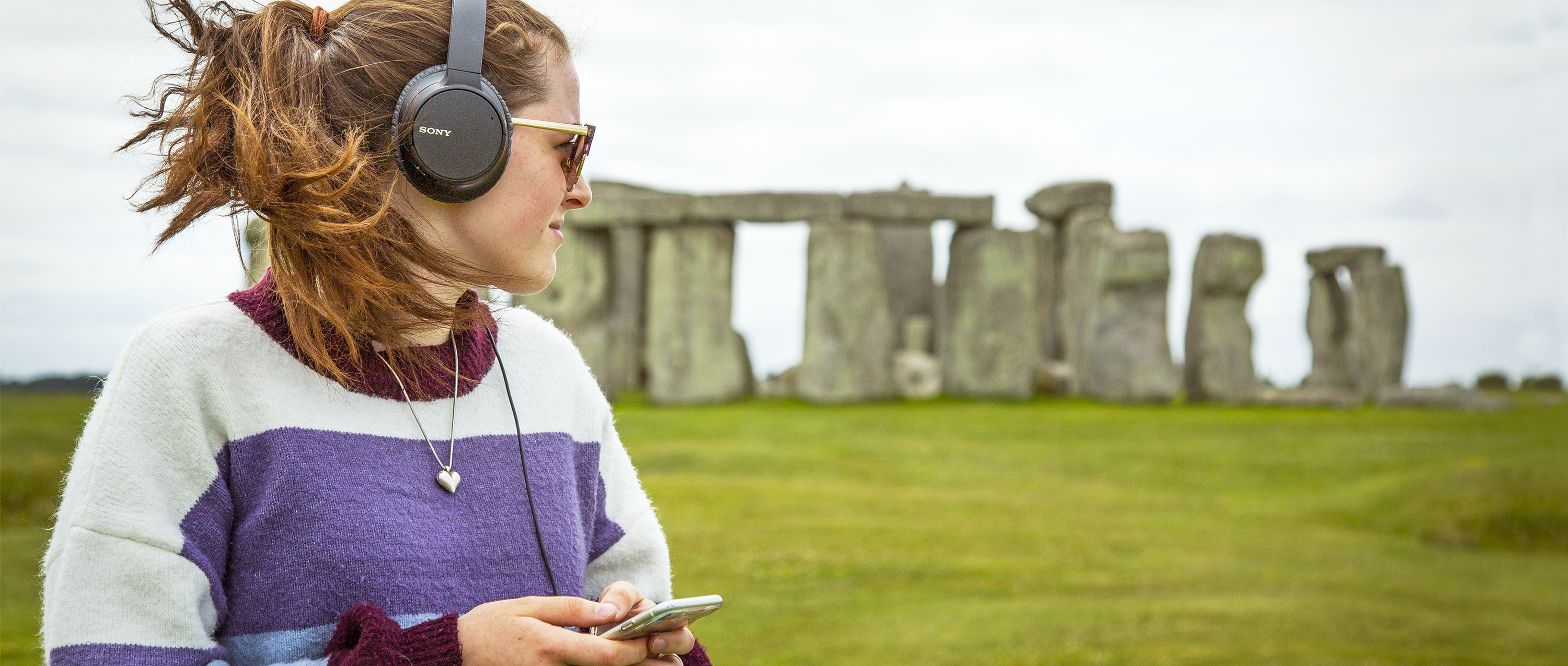 A woman listens to podcast episodes at Stonehenge