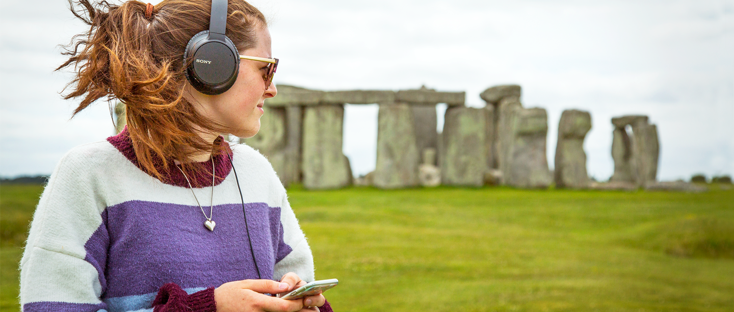 A woman listens to podcast episodes at Stonehenge