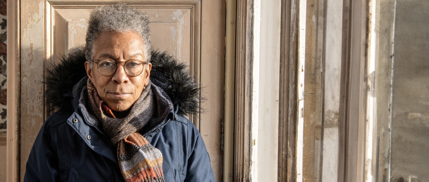 Photo of artist Ingrid Pollard MBE standing in a room in Belsay Hall in Northumberland