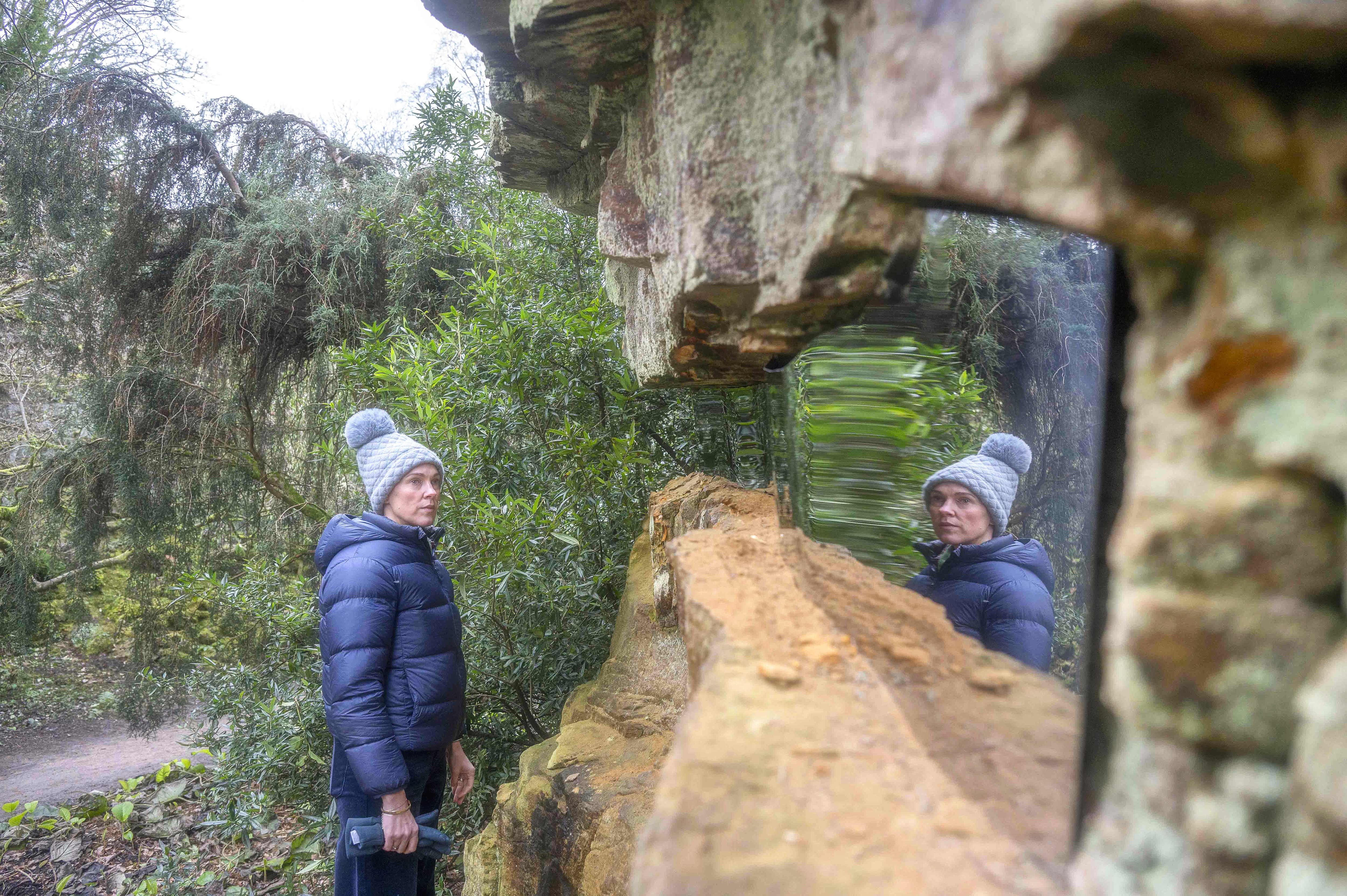 Photo of a person looking at a reflected surface inserted into the rock in the Quarry Garden at Belsay Hall, Castle and Gardens