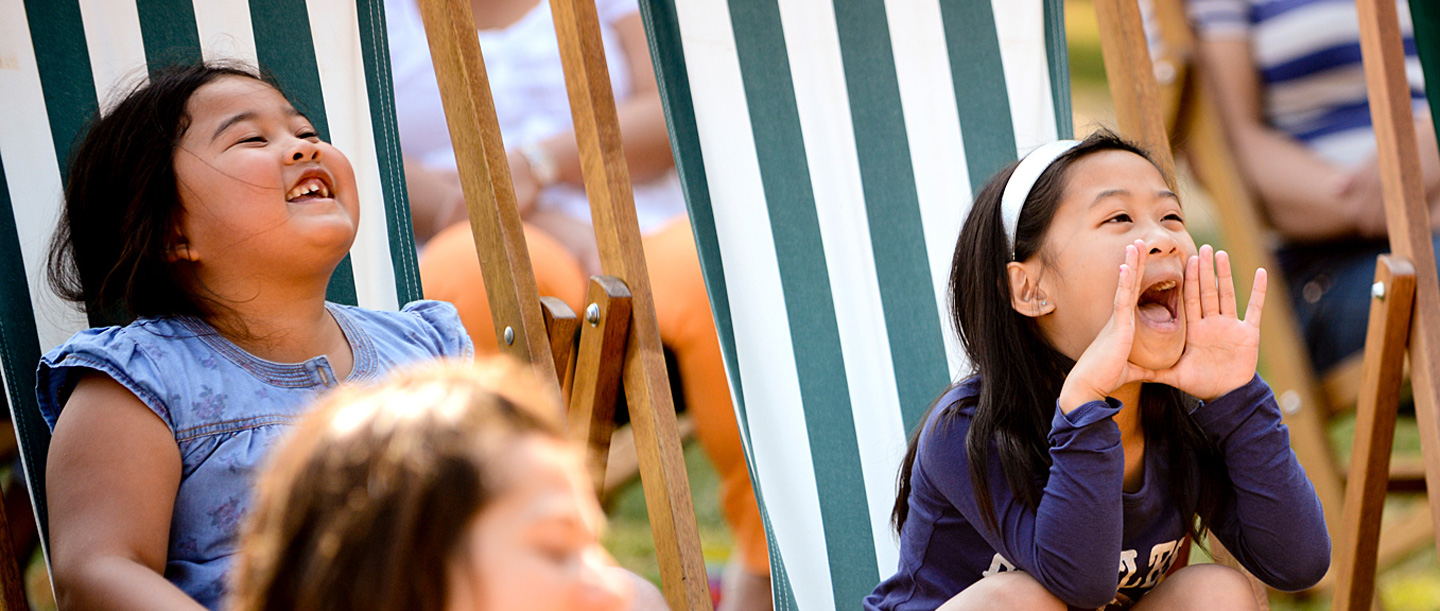 Two young children smile and shout as they sit on deck chairs at Osborne.