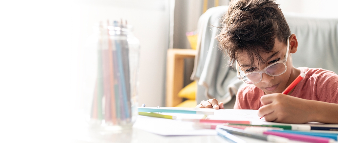 Image: Boy with glasses drawing with coloured pens