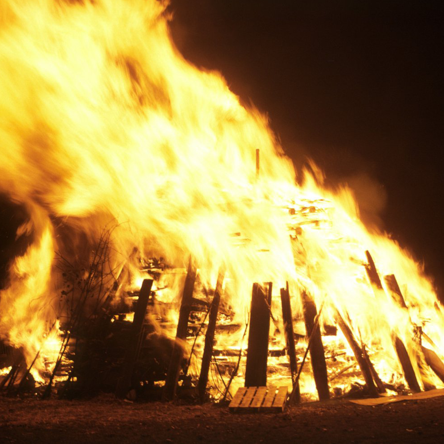 Image: a bonfire burning against a black sky