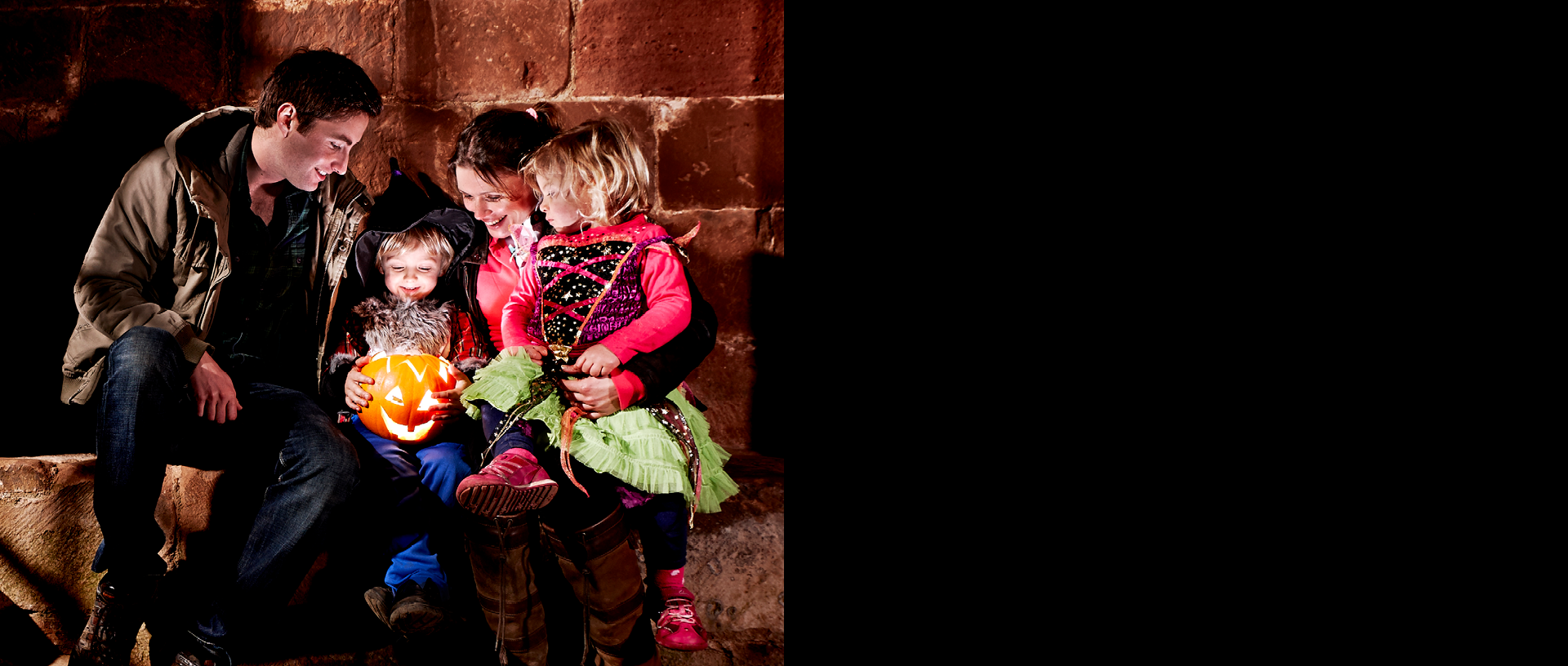 Image: a family are gathered around a glowing Halloween carved pumpkin