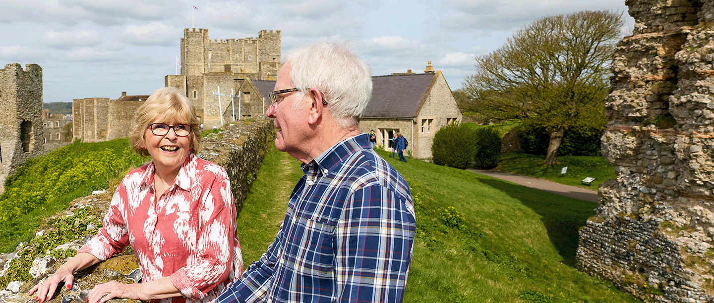 Photo of two people standing along a wall in the summer with Dover Castle in the background