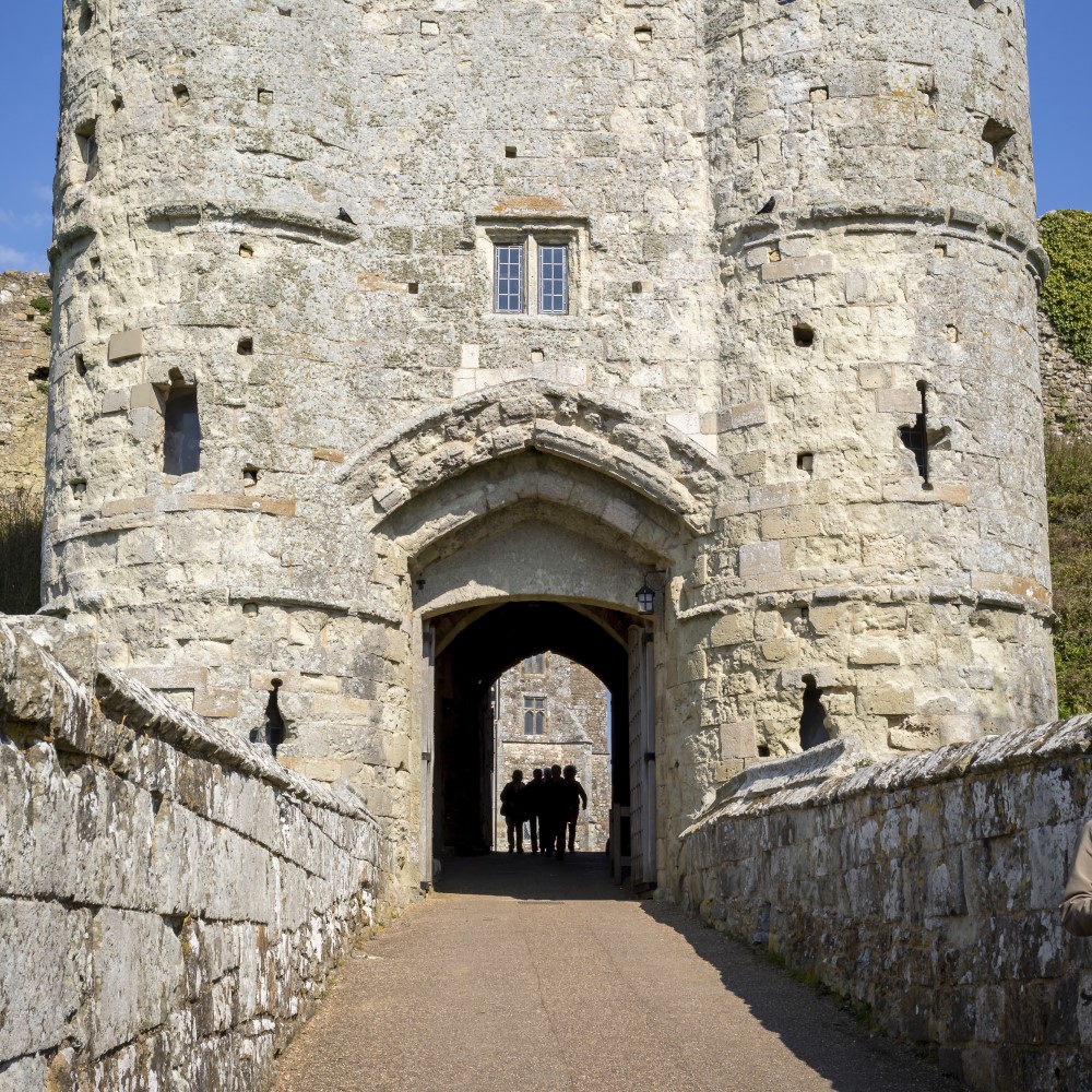 Photo of a group of people in silhouette walking through the gatehouse at Carisbrooke Castle on a sunny day