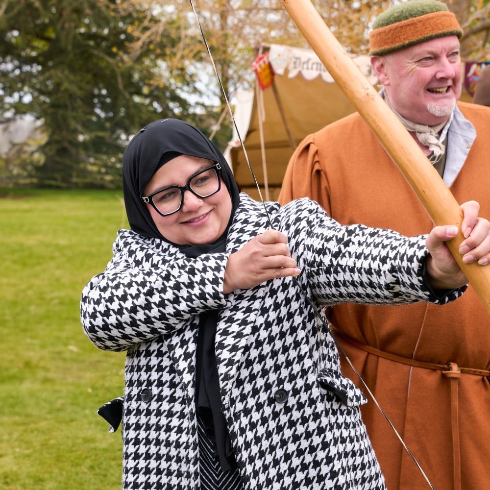 Photo of someone practising archery next to an instructor in medieval costume