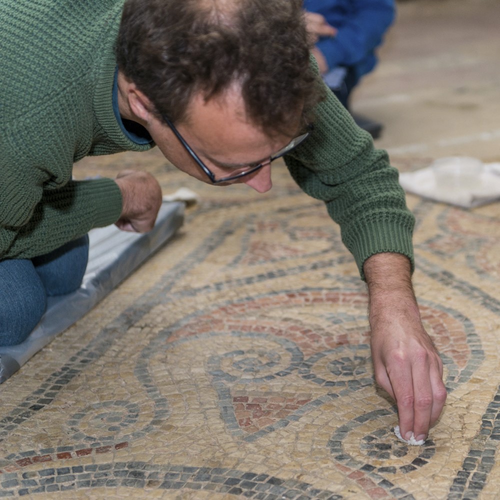 Photo of someone carefully cleaning a floor mosaic at North Leigh Roman Villa