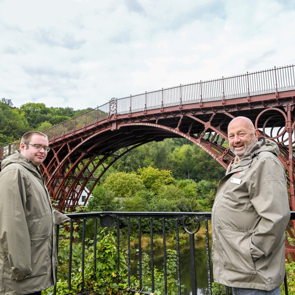 Photo of two English Heritage volunteers standing in front of Iron Bridge in Shropshire