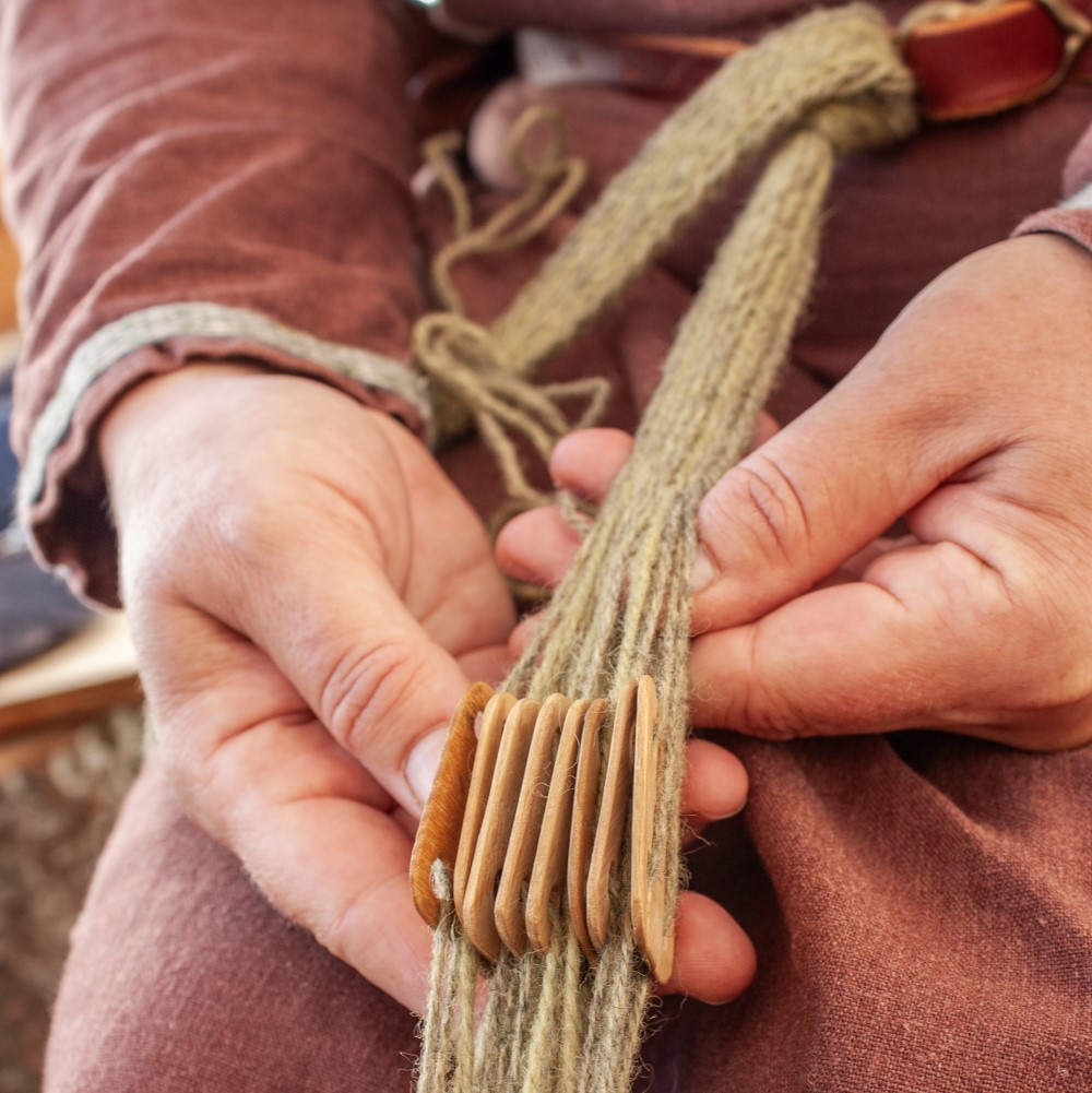 Photo of someone dressed in historical costume tablet-weaving
