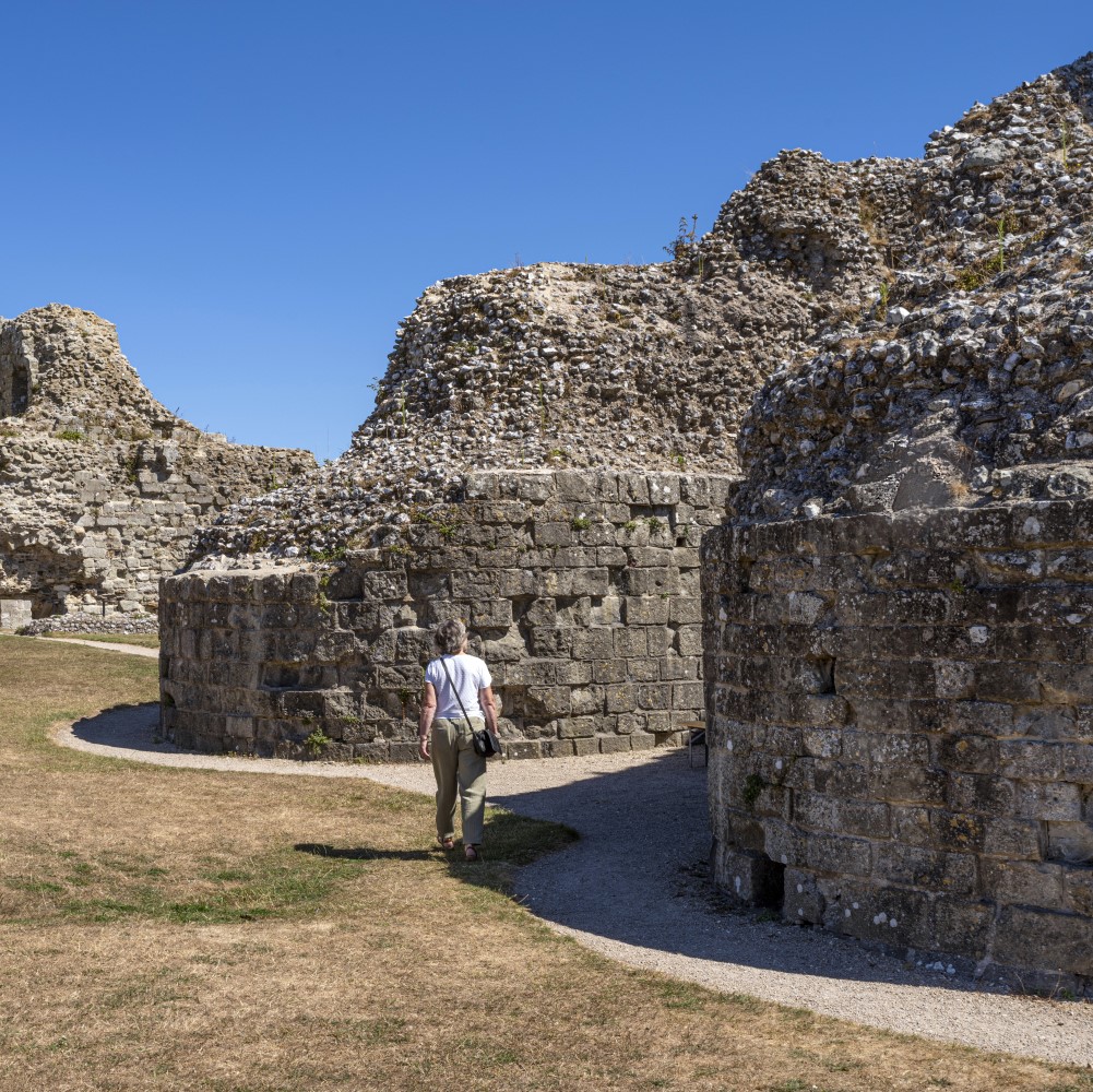 Photo of a visitor walking round the remains of Pevensey Castle on a sunny day