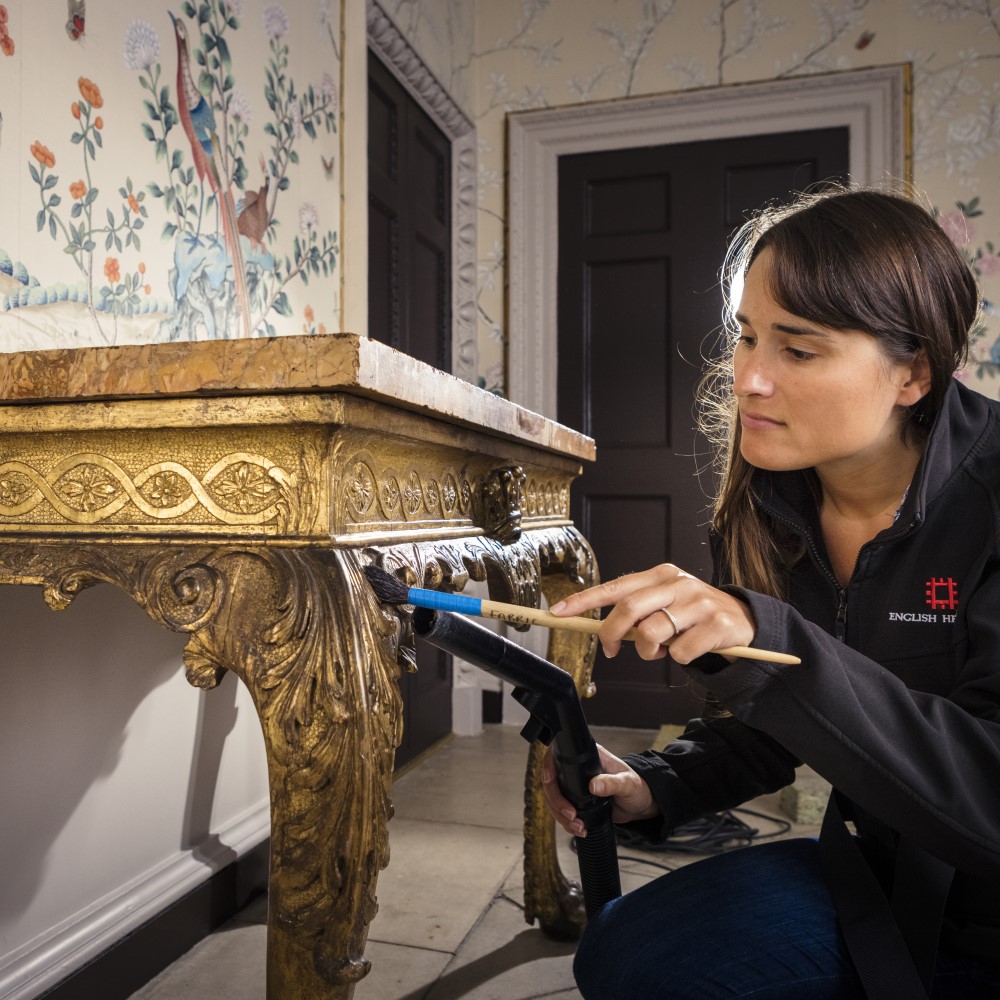 Photo of an English Heritage staff member cleaning a gold table with a brush at Marble Hill