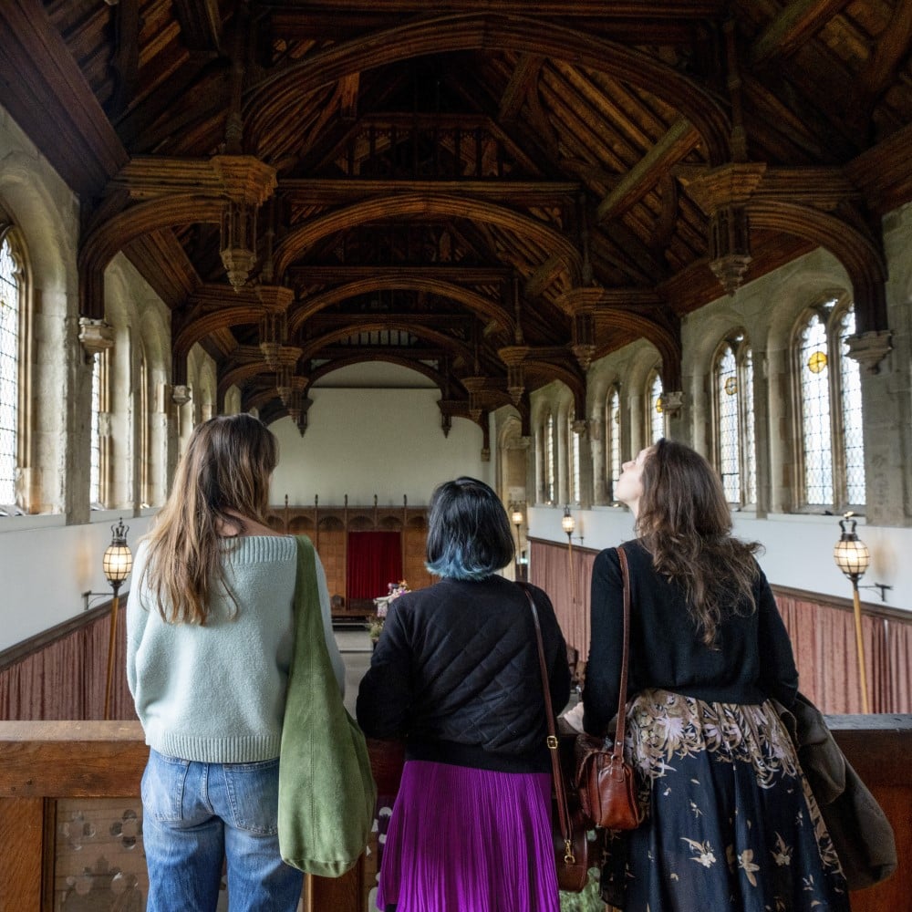 Photo of three people looking up at the wooden ceiling in a hall at Eltham Palace