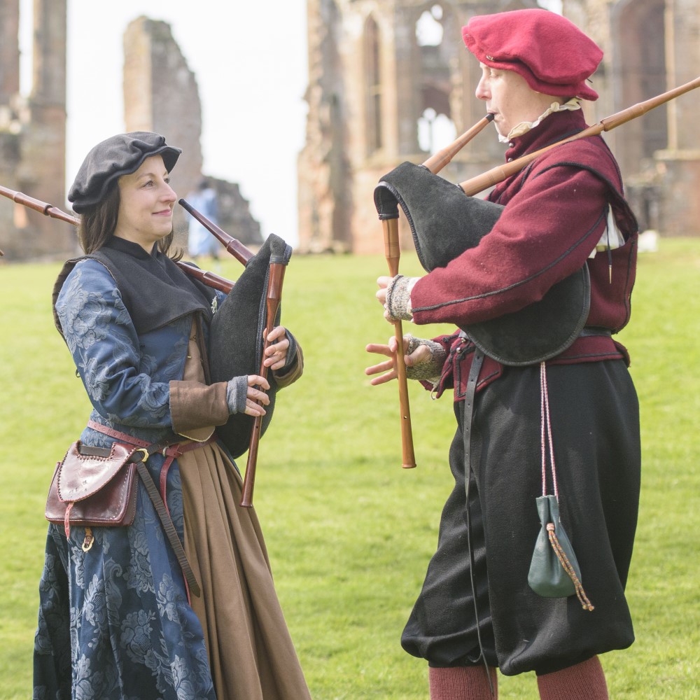 Photo of two people dressed in medieval costume and playing medieval bagpipe-like instruments