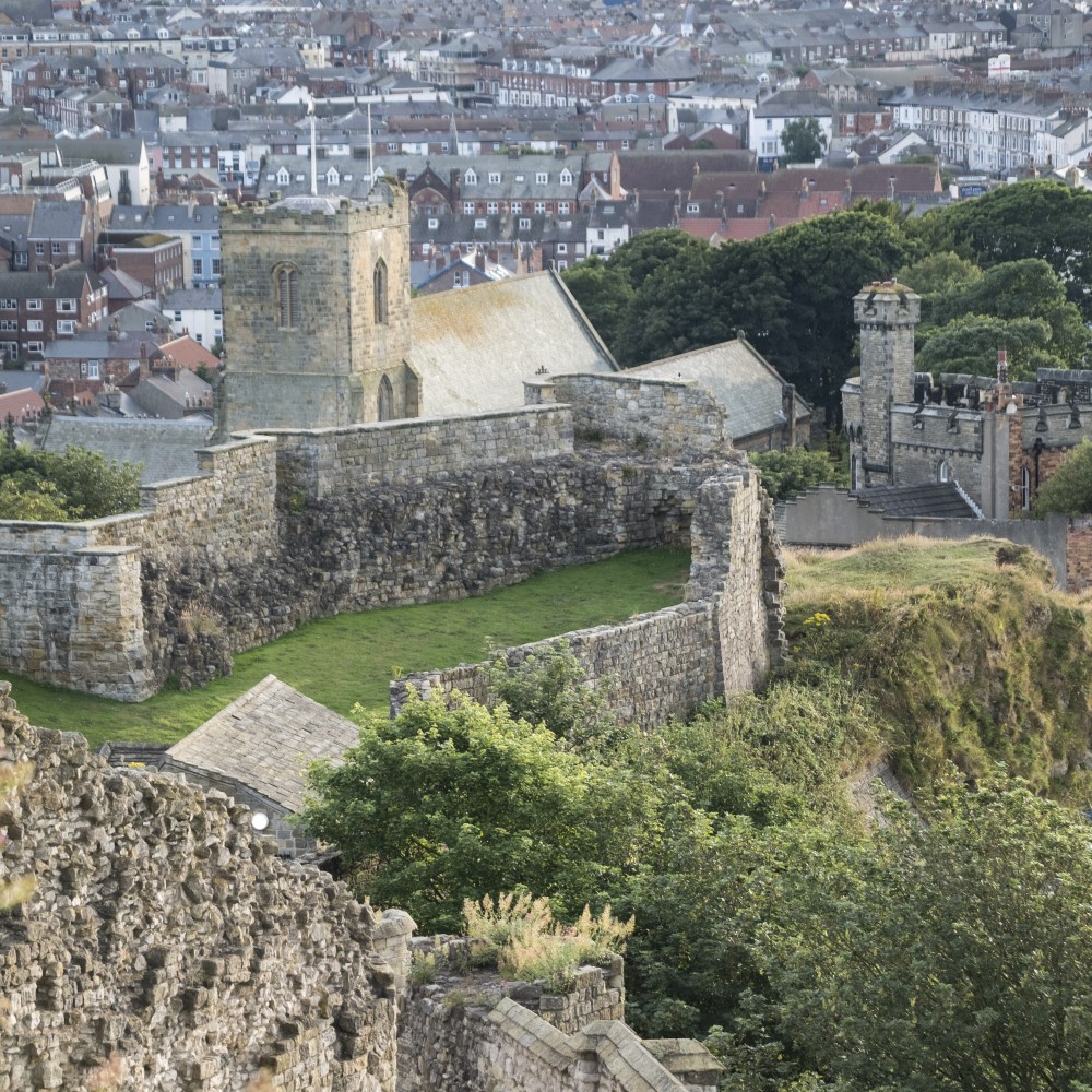 Photo of the walls of Scarborough Castle with a church and the town in the background