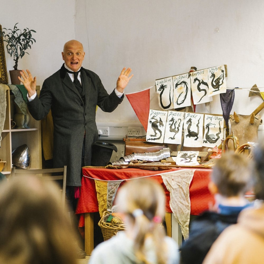 Photo of an adult dressed in Victorian costume speaking to a group of children