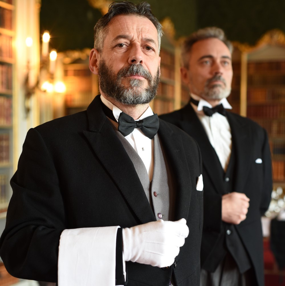 Photo of two people dressed as butlers in a historical library