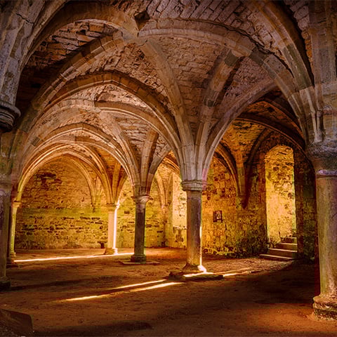 A room with lots of stone arches and a vaulted ceiling with a warm orange glow as sunlight creeps in a window