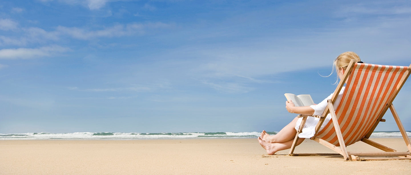 Photo of a person reading a book in a deckchair on a beach