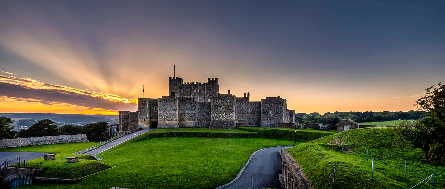 A view of Dover Castle underneath a dark sky with the sun setting.