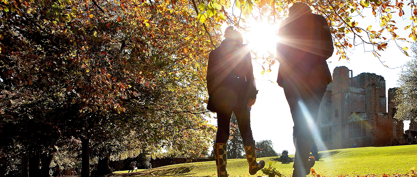 Photo of two people silhouetted against the sun in the autumn gardens of Kenilworth Castle in Warwickshire
