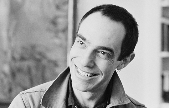 Black and white portrait photograph of Derek Jarman, smiling