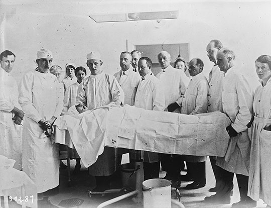 Black and white photograph of surgeon Harold Gillies and his team wearing white surgical gowns standing around a recumbent patient