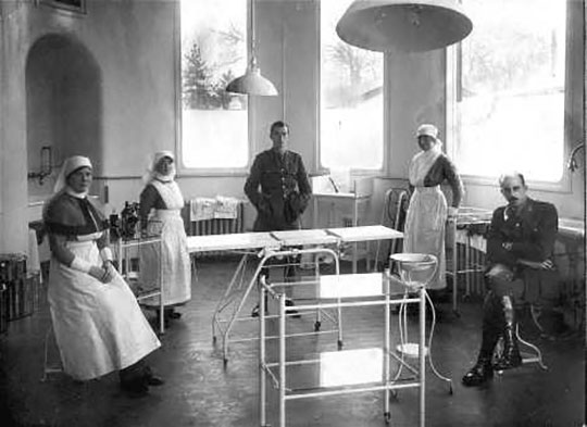 Black and white photograph of five people surrounding a gurney, three women in nurses' uniforms and two men (one of whom is surgeon Harold Gillies) in military uniforms.
