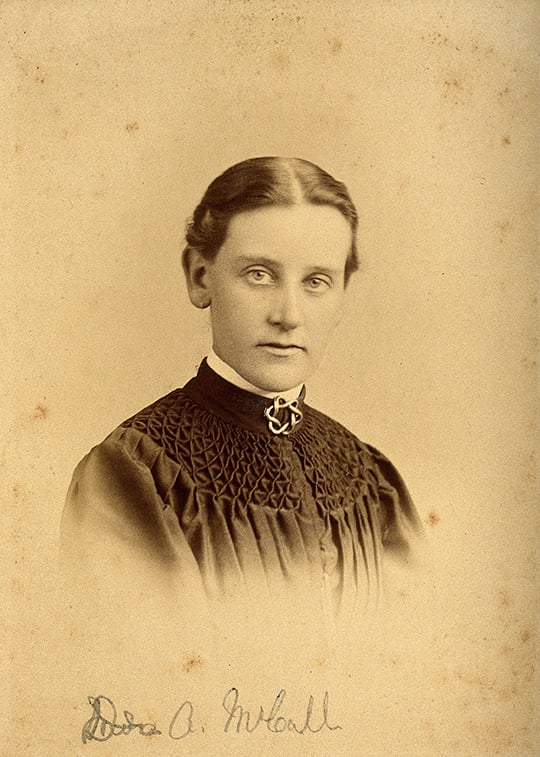 Sepia-toned portrait of Dr Annie McCall with a black smocked dress, brooch at her throat and parted, tied-back dark hair