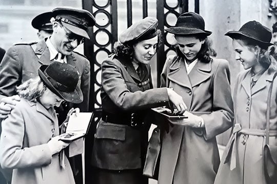 Black and white photograph of Sansom with her children, looking at her medals outside the gates of Buckingham Palace Black and white photograph of Sansom with her children, looking at her medals outside the gates of Buckingham Palace